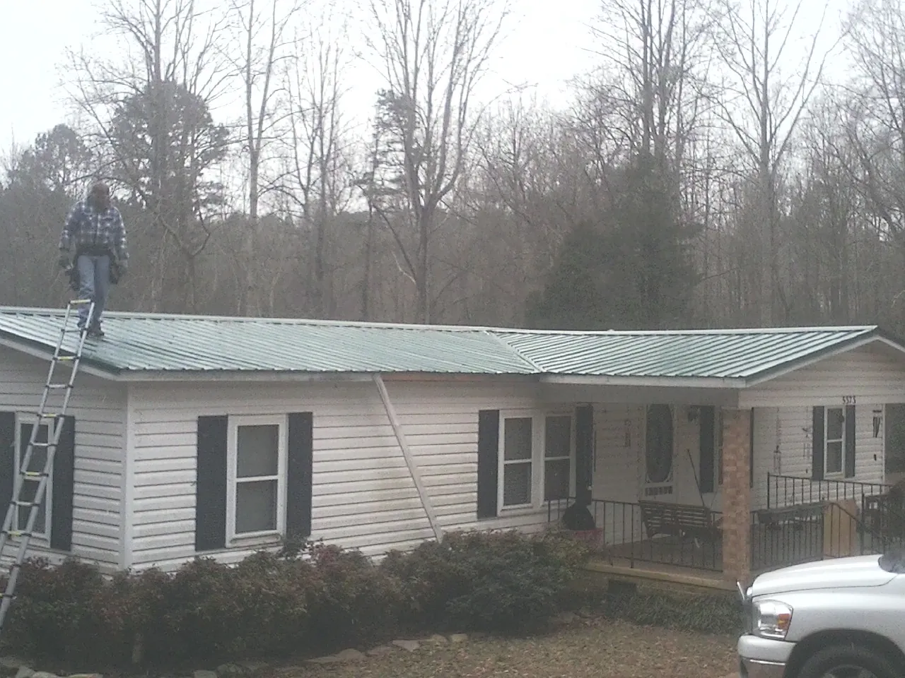 Worker on a ladder beside a new green metal roof on a ranch home in Prospect