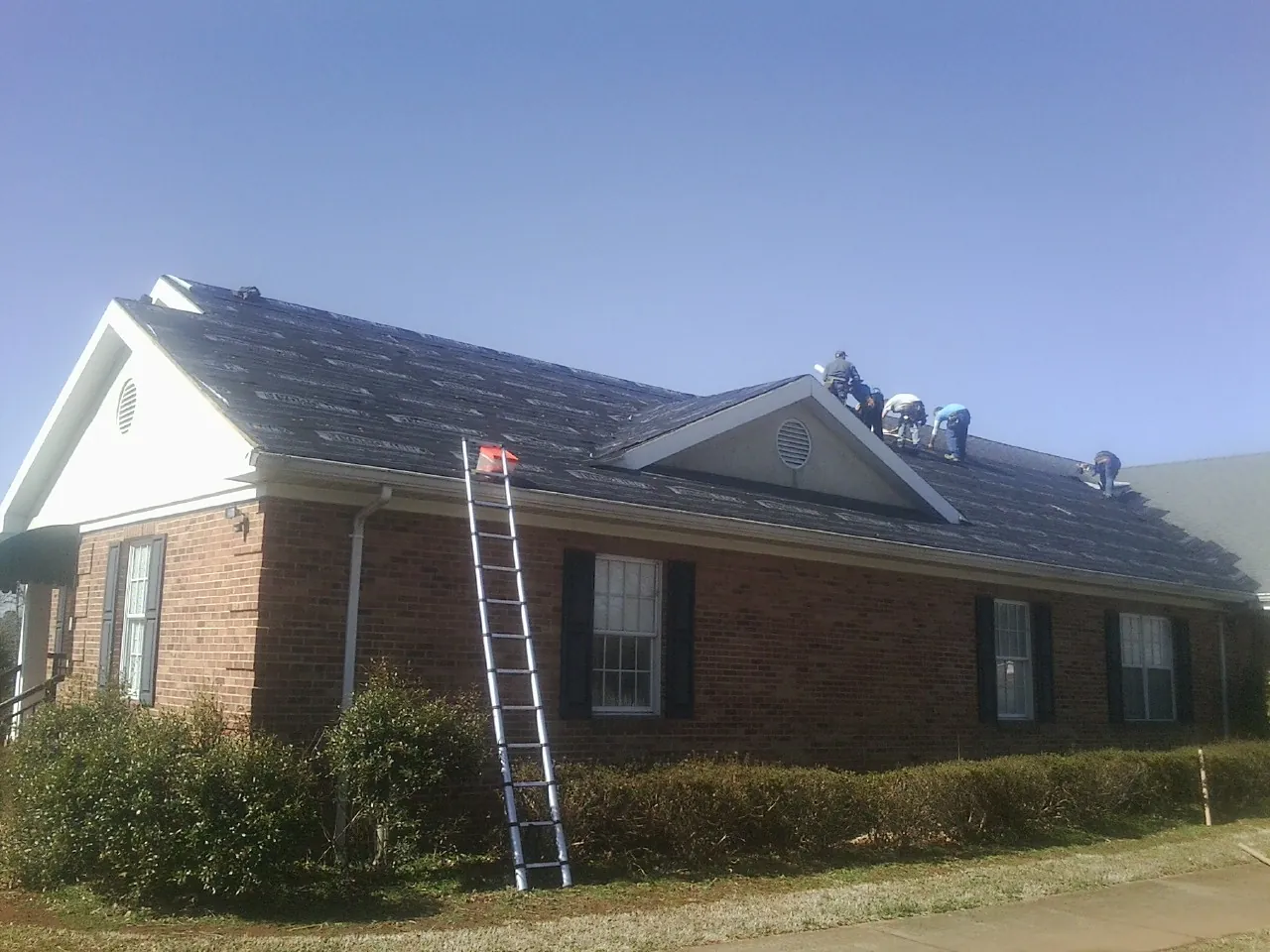 Crew tearing shingles off a brick ranch roof with a ladder set — Emergency Roof Repair work by our crew in Prospect